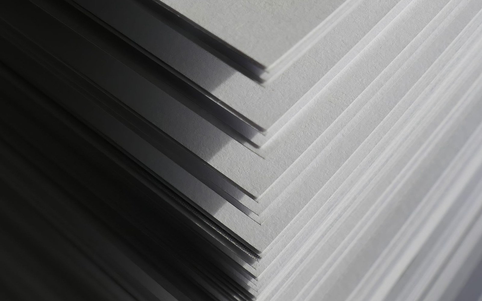Three sheets of off-white paper stacked at slight angles, casting layered shadows between them in side light